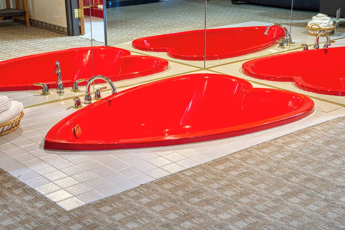 Une baignoire rouge dotée de plusieurs robinets et posée sur un sol carrelé.