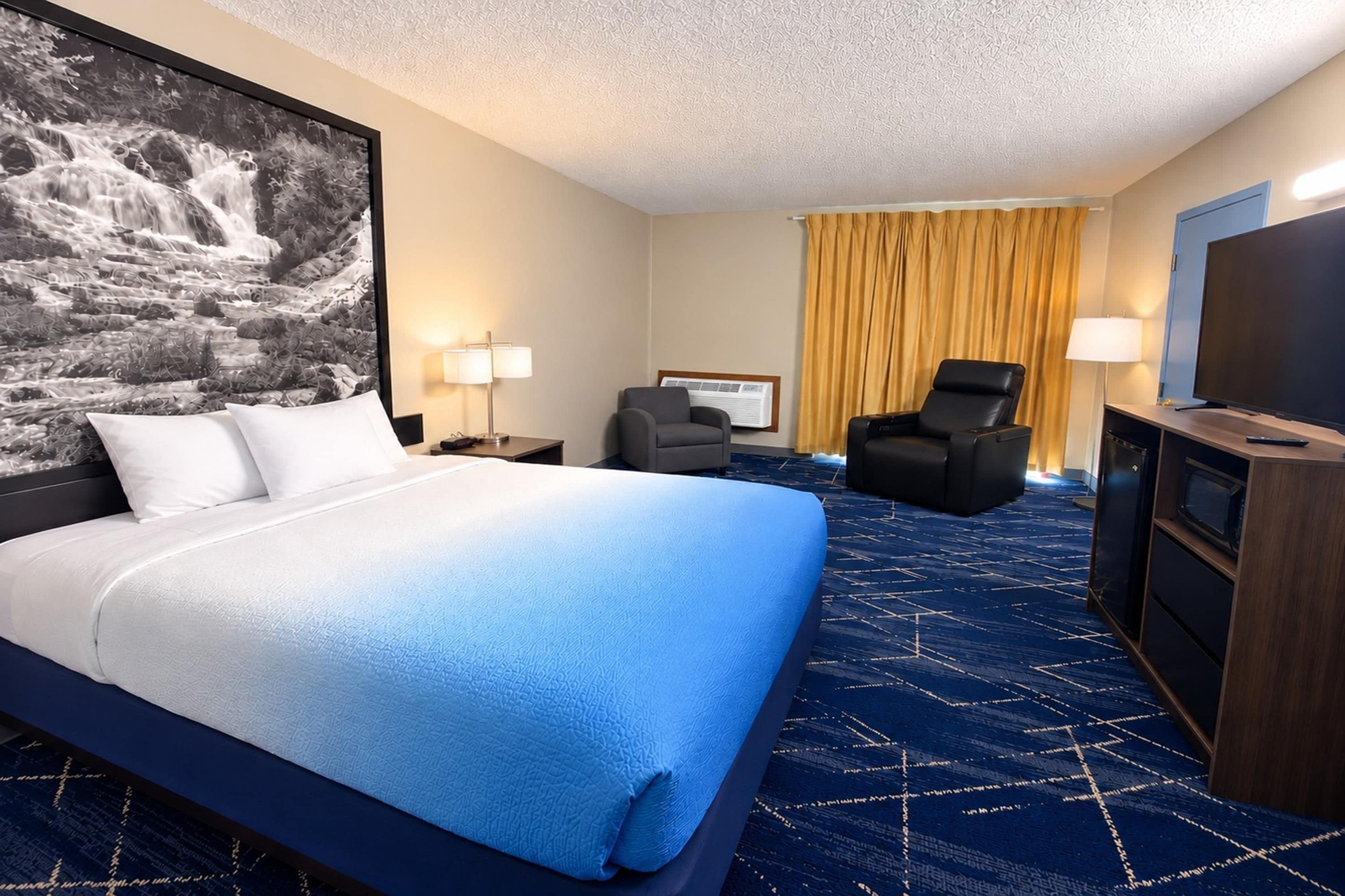 Une chambre d’hôtel avec un grand lit, un téléviseur à écran plat, un bureau, une chaise et une grande fenêtre avec des rideaux.