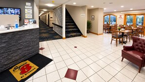 A hotel lobby with a reception desk, a staircase, and a dining area with tables and chairs.