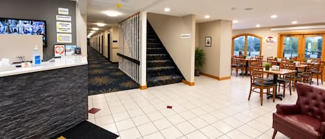 A hotel lobby with a reception desk, a staircase, and a dining area with tables and chairs.