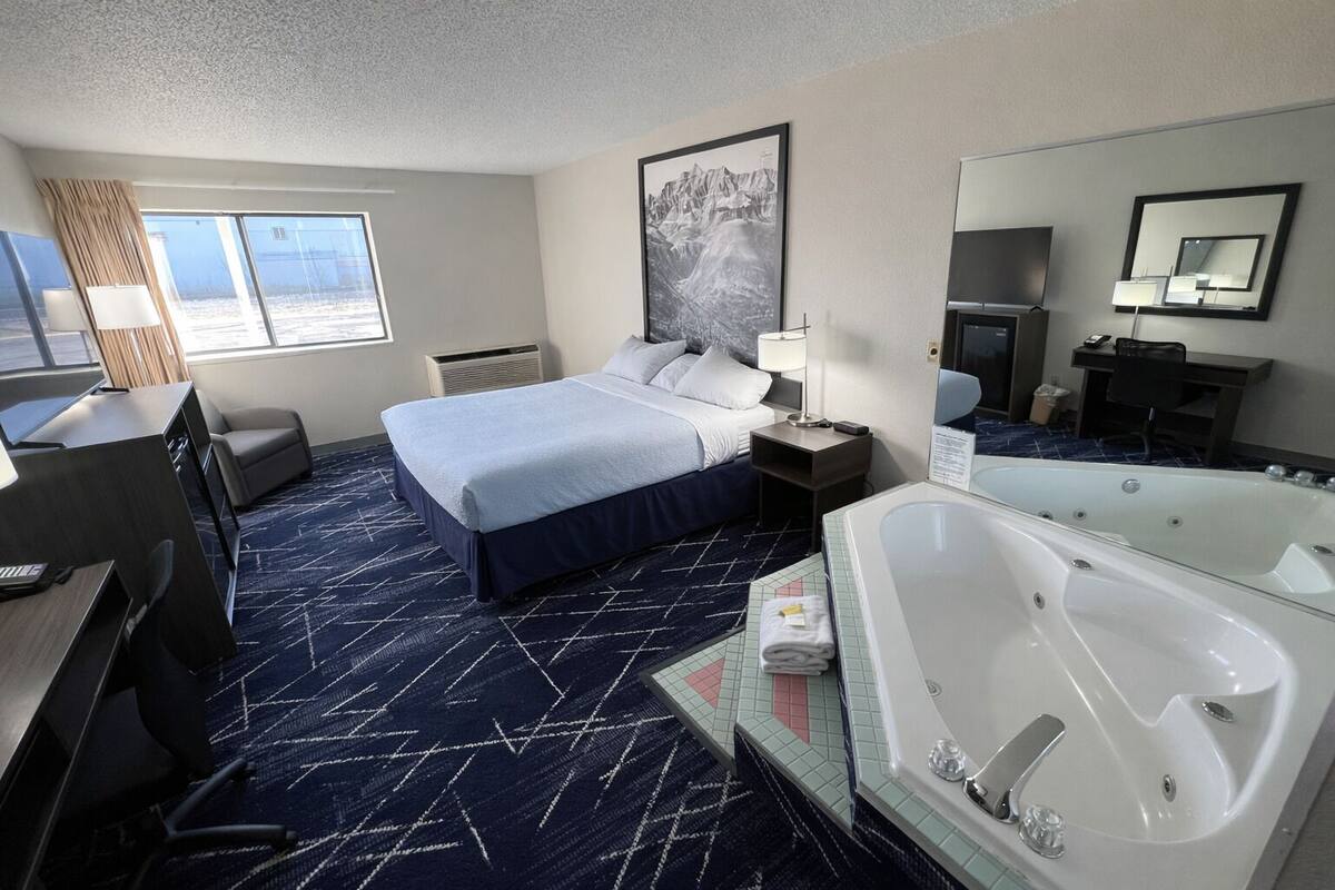 Une chambre d’hôtel avec un lit, un bureau, une chaise et une grande baignoire.