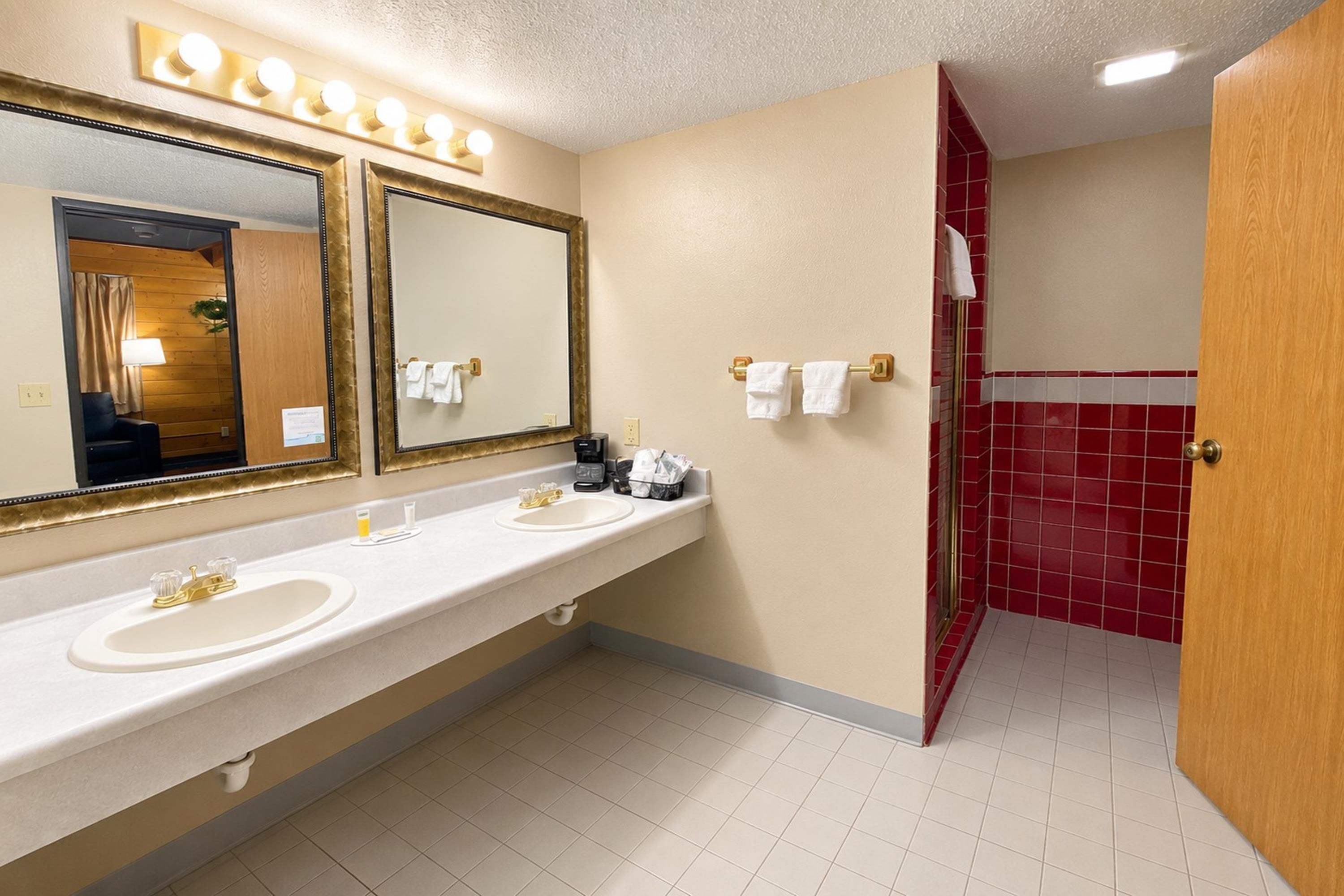 A hotel bathroom with a double sink, a large mirror, and a red-tiled shower area.