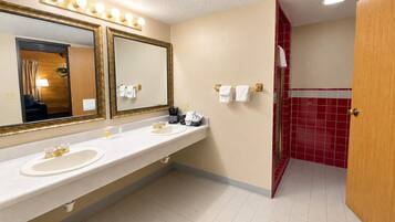 A hotel bathroom with a double sink, a large mirror, and a red-tiled shower area.