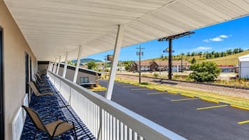 Un espace extérieur abrité, aménagé avec des rangées de chaises, offrant une vue sur un parking et sur un bâtiment situé à l'arrière-plan.