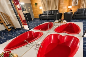 Une chambre d’hôtel avec une grande baignoire en forme de cœur, un canapé et un miroir.