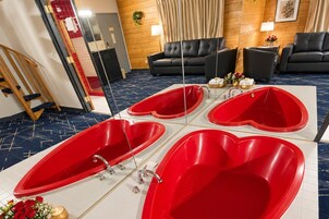 Habitación de hotel con una tina en forma de corazón, un sofá y un espejo.