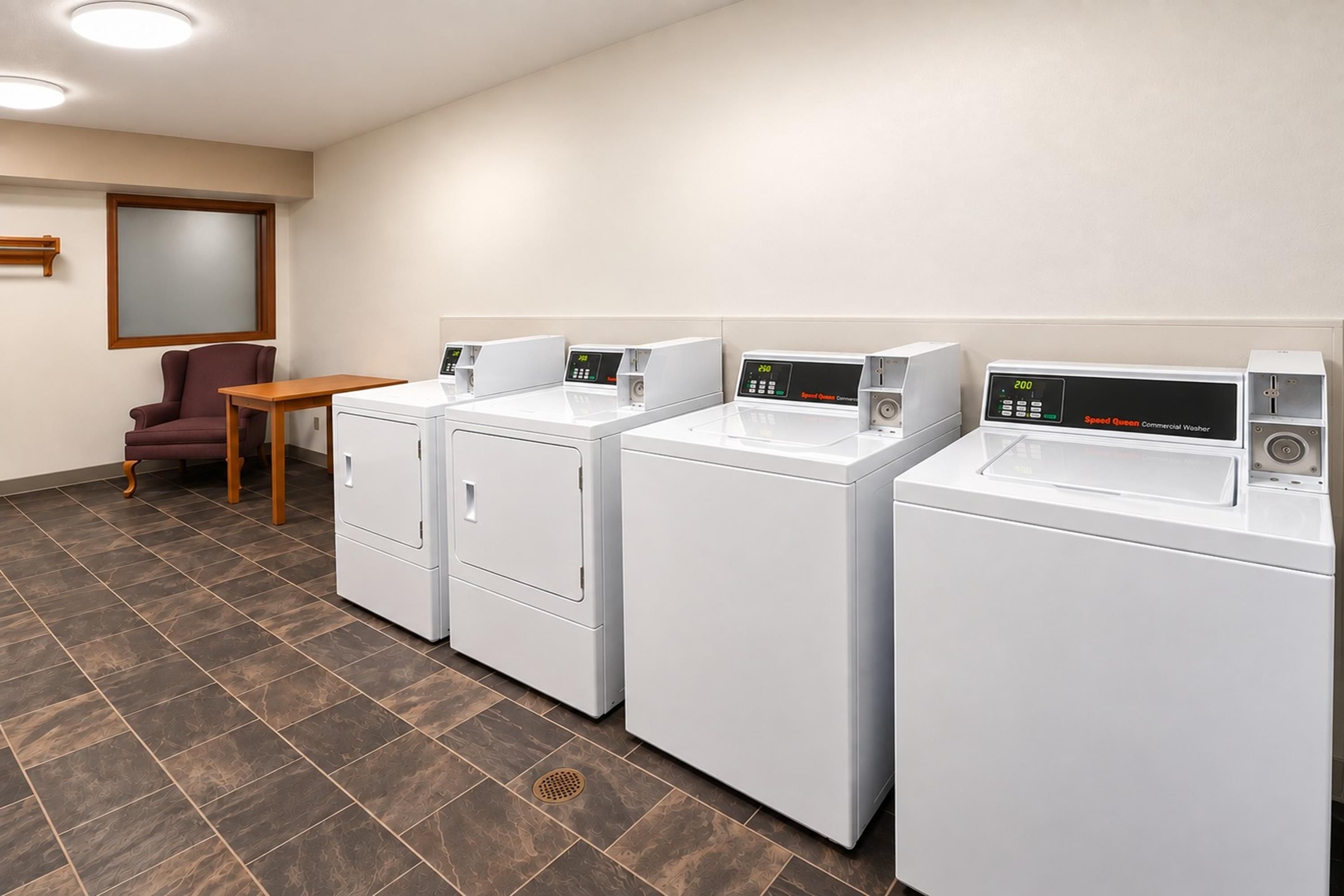 Een wasserette met vier witte wasmachines, een houten tafel en een paarse stoel.