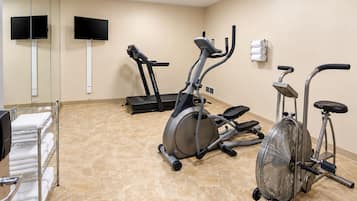 Un gimnasio con equipo de ejercicio, un televisor y un perchero para toallas.