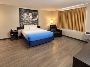Une chambre d’hôtel comprenant un lit, une table de chevet, une chaise, une lampe fixée au mur et une fenêtre avec des rideaux.