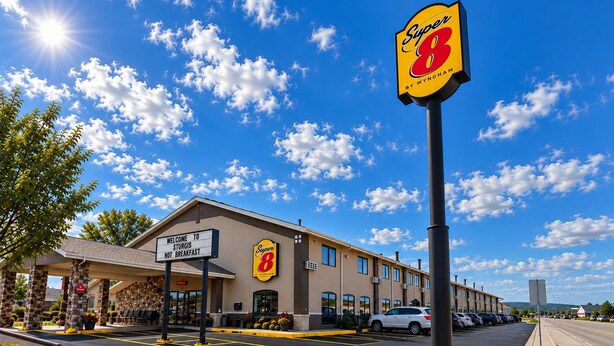 A Super 8 hotel with a clear sky, a parking lot, and a sign indicating it's not breakfast.
