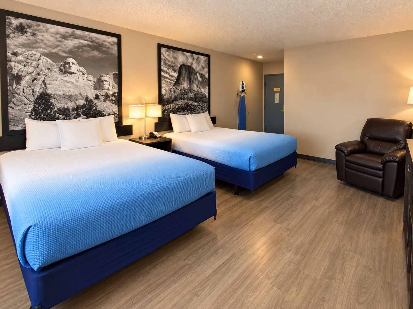 A hotel room with two beds, a chair, and artwork on the walls.