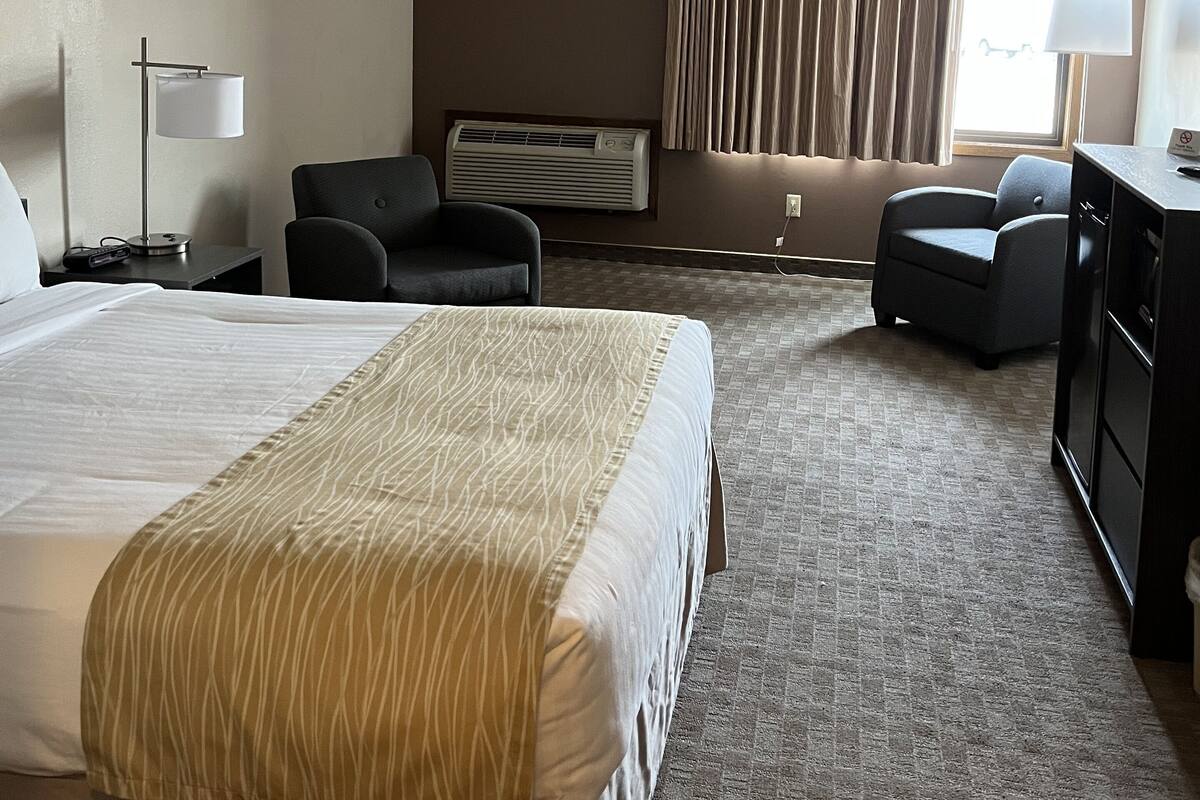 Une chambre d’hôtel avec un grand lit, un bureau, une chaise, un canapé, une commode et une fenêtre avec des rideaux.