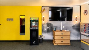 A room with a yellow wall, a large flat-screen TV, a wooden dresser, and a gaming console.