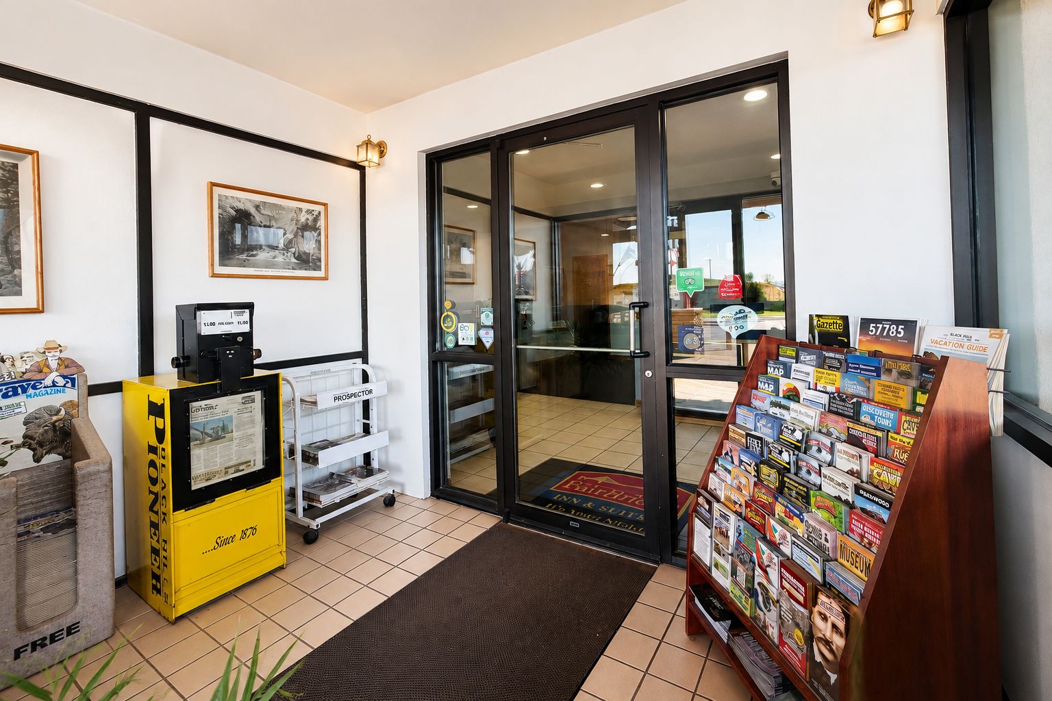 A hotel lobby with a reception desk, a magazine rack, and a door leading to the dining area.