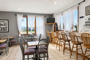 Un comedor con mesas y sillas, un televisor y ventanas con cortinas.