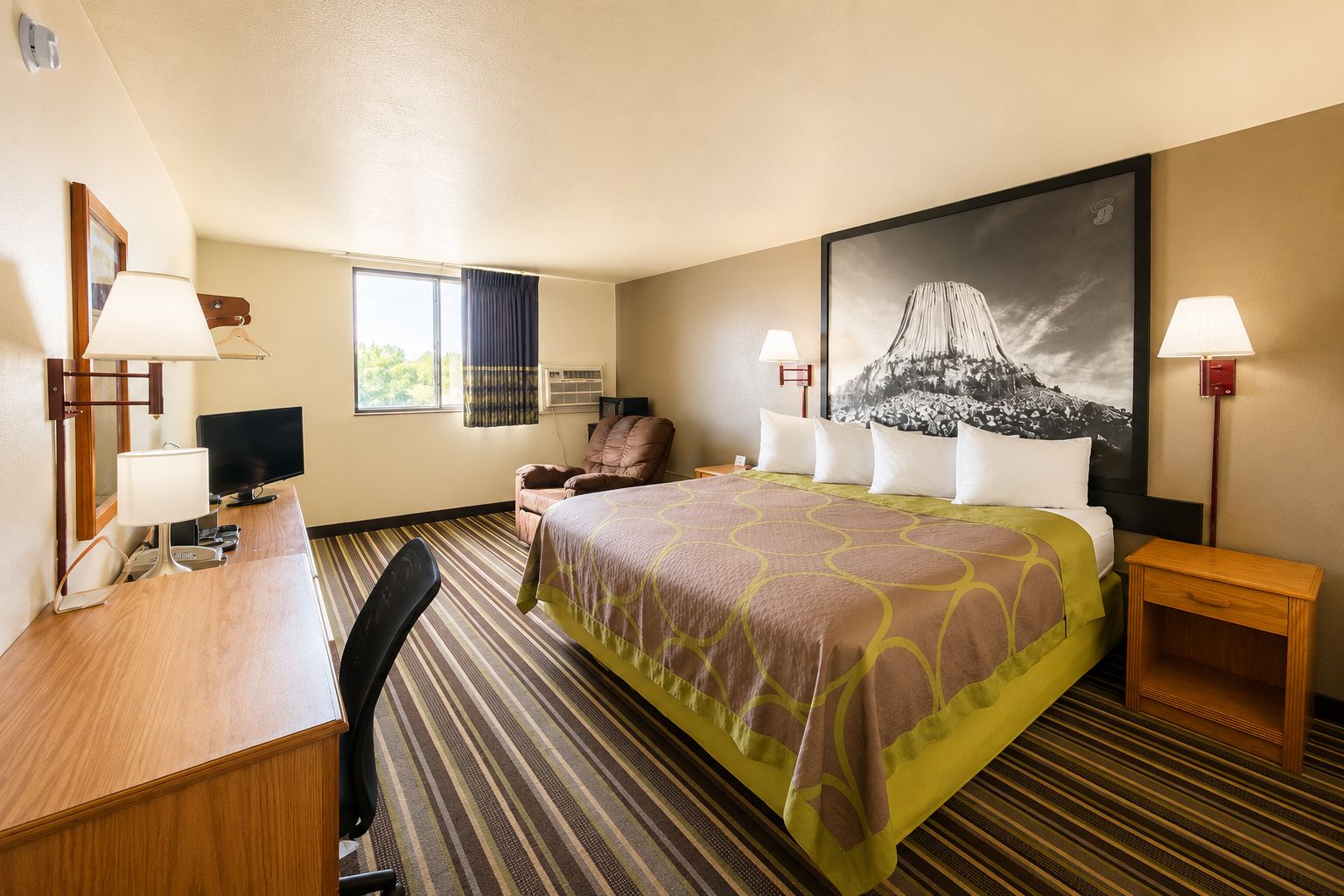 Une chambre d’hôtel comprenant un lit, un bureau, une chaise, une télévision, une fenêtre avec des rideaux et un grand tableau accroché au mur.