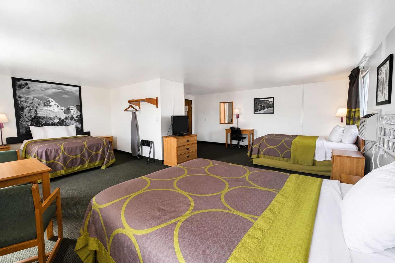 Ett hotellrum med två sängar, ett skrivbord, en stol, en byrå, en tv och en stor, inramad tavla på väggen.
