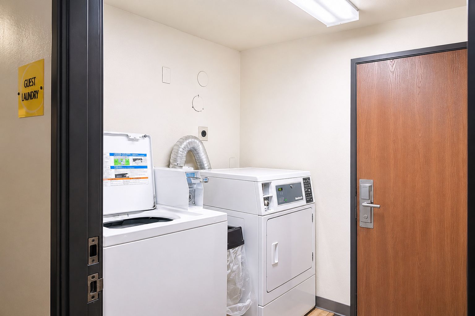 A laundry room with a sign indicating guest laundry facilities, a dryer, a washing machine, and a wooden door.
