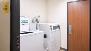 A laundry room with a sign indicating guest laundry facilities, a dryer, a washing machine, and a wooden door.