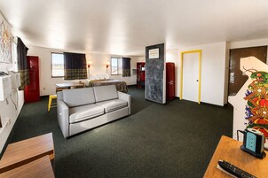 Habitación de hotel con sofá, mesa de comedor, cama, escritorio con computadora y televisor.