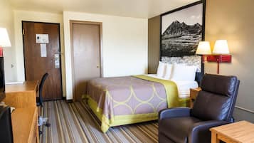 Habitación de hotel con cama, escritorio, silla, lámpara y un cuadro en la pared.