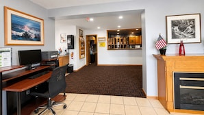 A hotel lobby with a reception desk, a computer station, a fire extinguisher, and framed artwork on the walls.