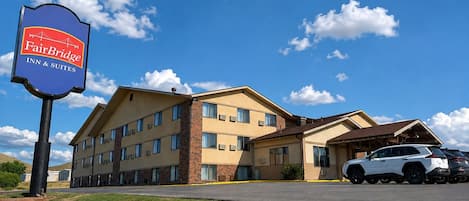 Un FairBridge Inn & Suites con estacionamiento y un SUV blanco estacionado al frente.