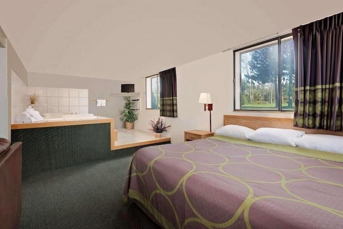 A hotel room with a bed, a desk, a chair, a lamp, and a window.