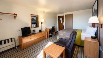 Una habitación de hotel con cama, escritorio, silla, televisor, lámpara y ventana.
