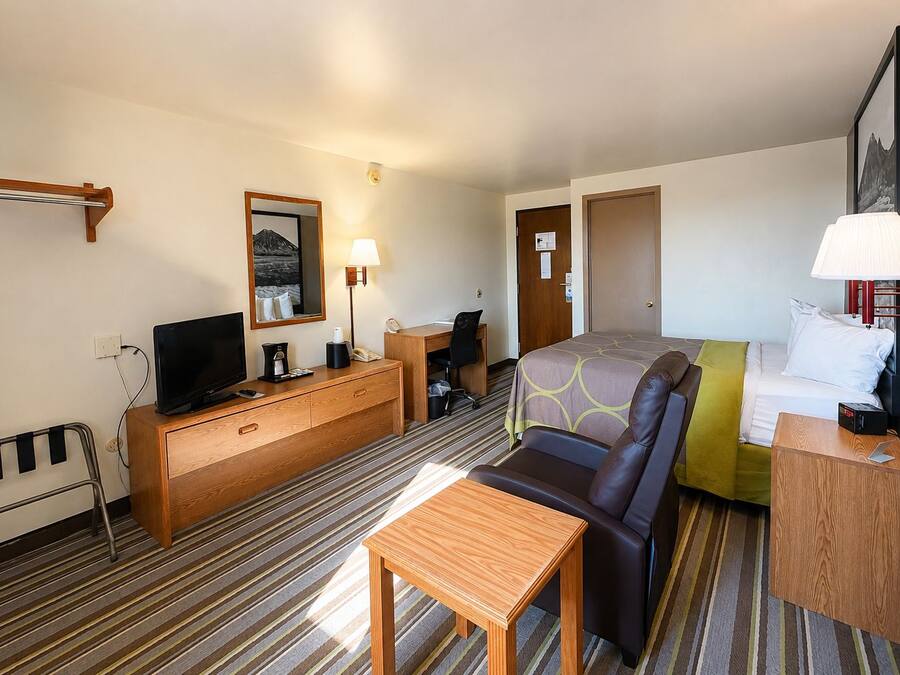Een hotelkamer met een bed, een bureau, een stoel, een televisie, een lamp en een raam.