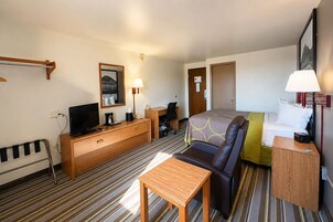 Una habitación de hotel con cama, escritorio, silla, televisor, lámpara y ventana.