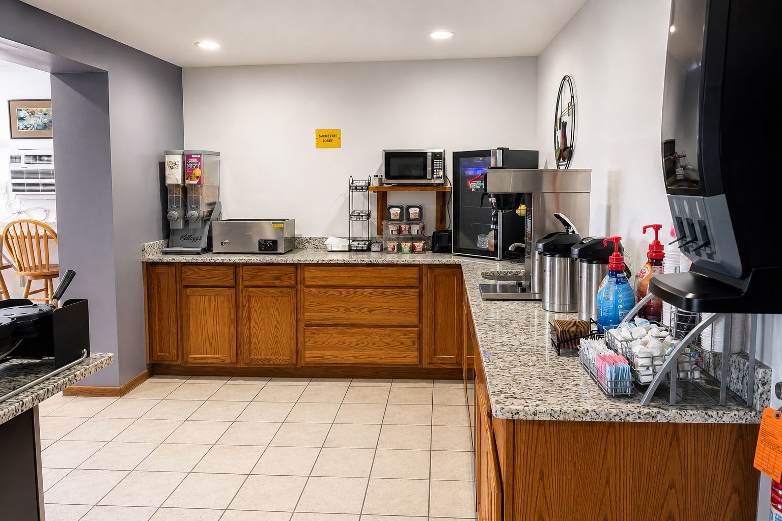 A modern kitchen with a granite countertop, wooden cabinets, a coffee machine, a microwave, and a refrigerator.