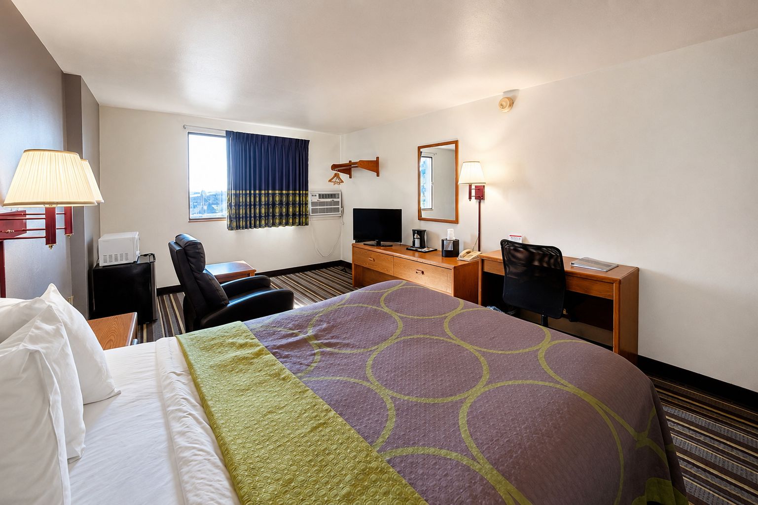 A hotel room with a bed, a desk, a chair, a television, and a window with curtains.