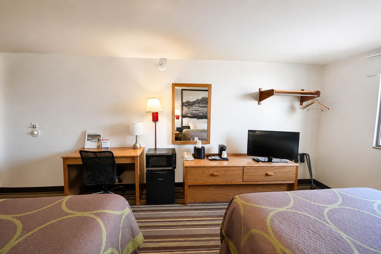 Habitación de hotel con escritorio, computadora, televisor, microondas, cafetera y teléfono, además de dos camas.