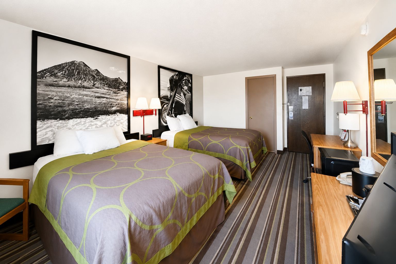 A hotel room with two beds, a desk, a chair, a television, and a bathroom door.