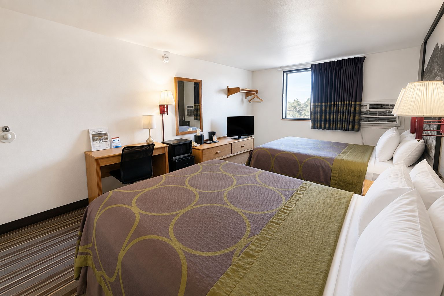 A hotel room with two beds, a desk with a computer, a mirror, and a window with curtains.