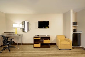 Une chambre d’hôtel équipée d’un bureau, d’une chaise, d’une télévision et d’une petite kitchenette.
