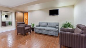 A living room with a brown sofa, a patterned sofa, and a striped armchair. There is a potted plant and a flat-screen TV on the wall. - Super 8 by Wyndham Lexington/Hamburg Area (Lexington)
