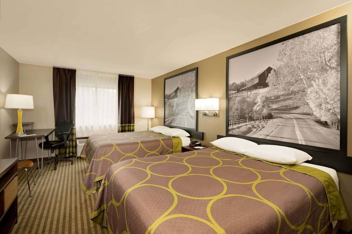 A hotel room with two beds, a desk, a chair, and two lamps.