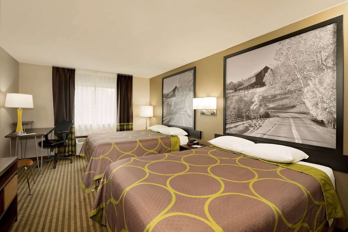 A hotel room with two beds, a desk, a chair, and a large framed picture on the wall.