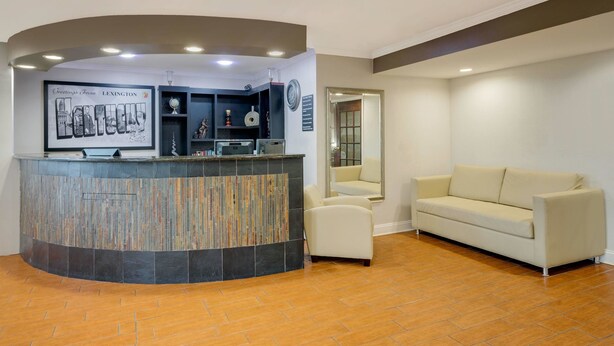 A reception area with a curved reception desk, a beige sofa, and a tiled floor. - Super 8 by Wyndham Lexington/Hamburg Area (Lexington)
