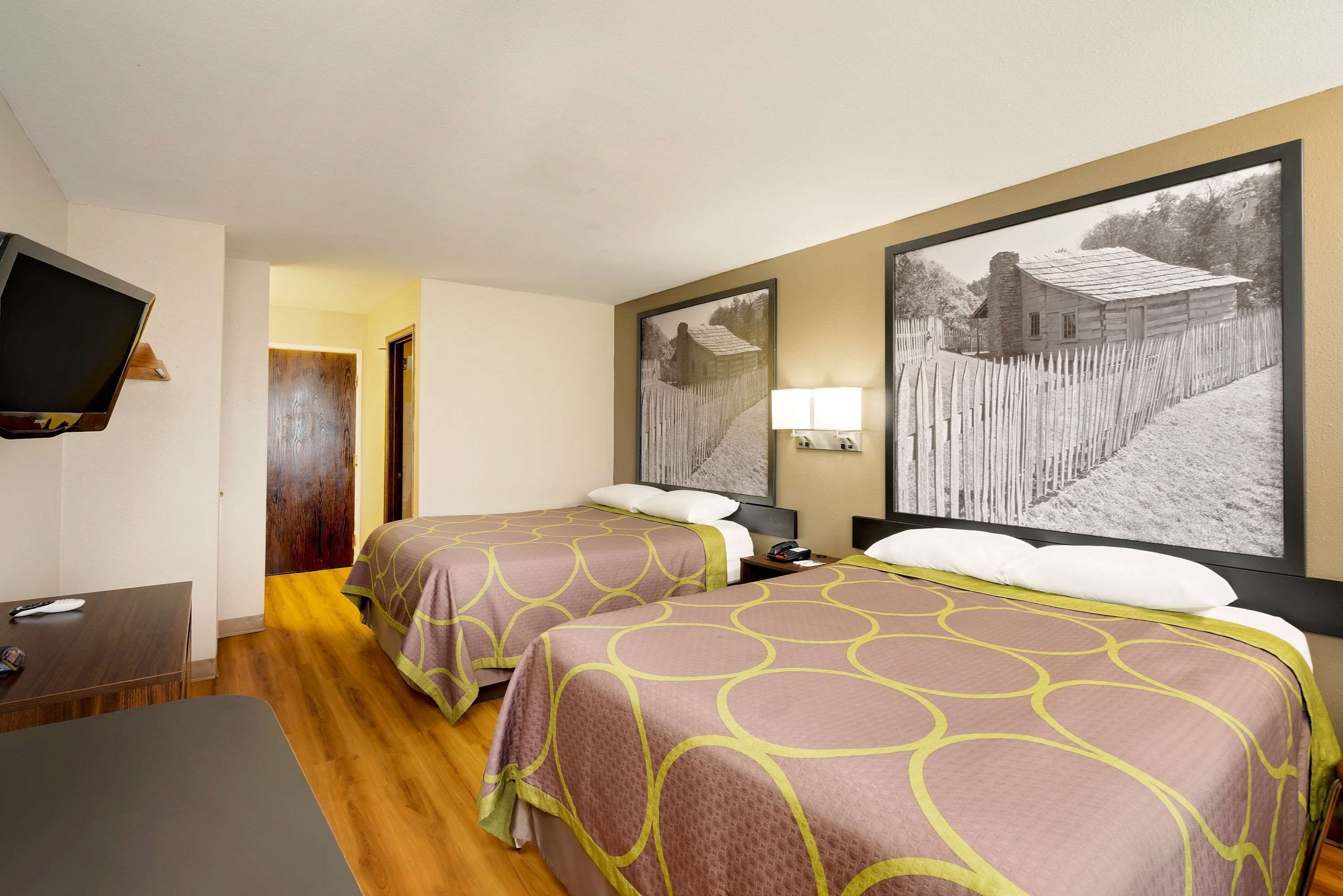 Habitación de hotel con dos camas, un televisor, un escritorio y un cuadro grande en la pared.