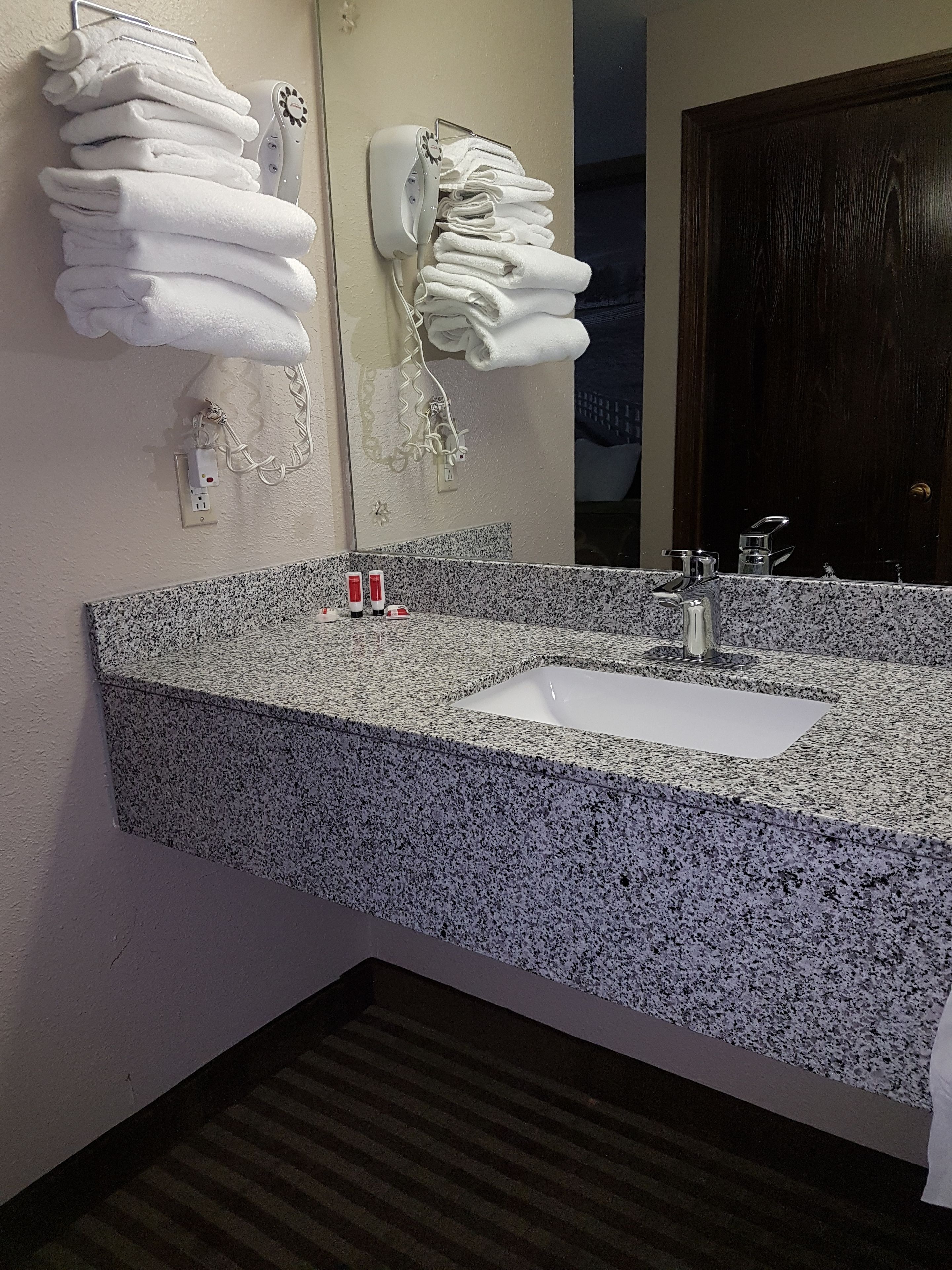 A bathroom with a granite countertop sink, two red and white toiletries, and towels hanging on a rack.