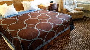 A hotel room with a large bed, a wooden headboard, a chair, a nightstand, and a window with an air conditioner. - Auburn Inn (Auburn)