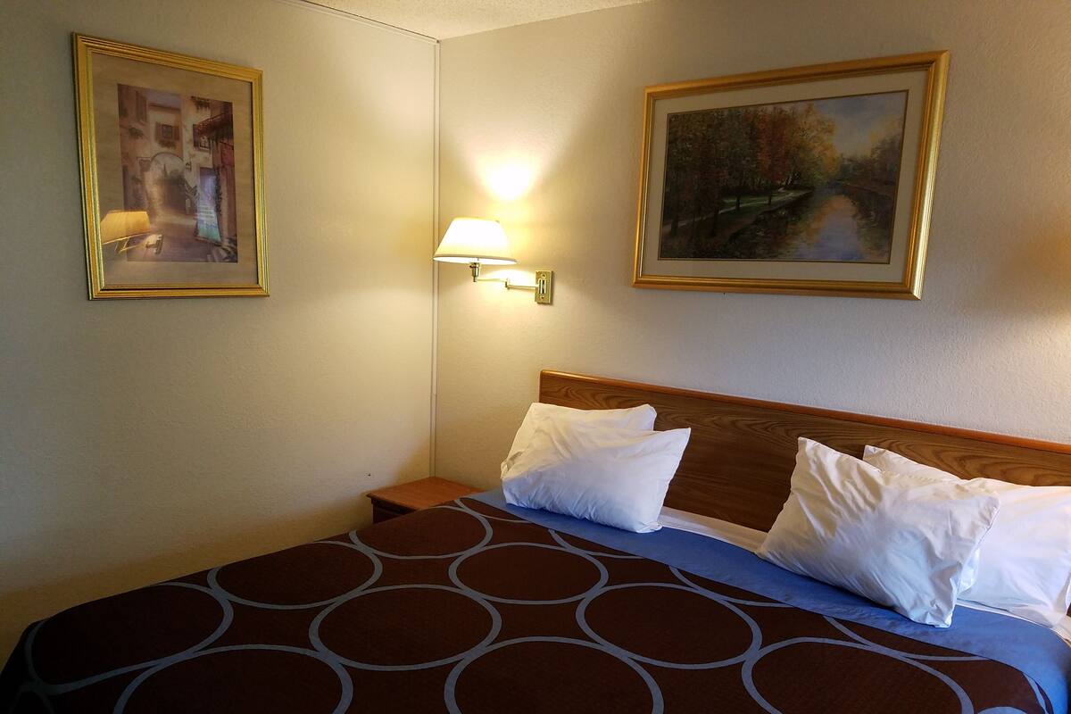 A hotel room with a bed, a nightstand, a lamp, and two framed pictures on the walls.