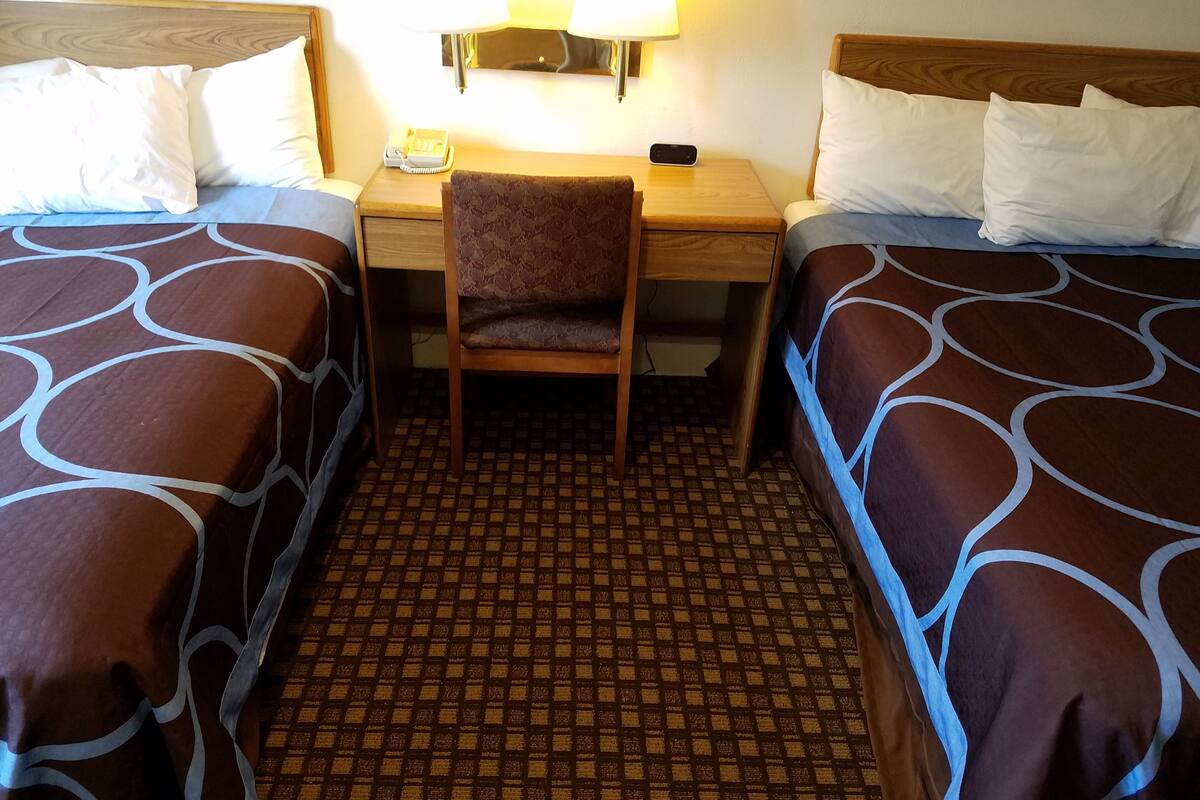 A hotel room with two beds, a desk, a chair, a lamp, and a phone.