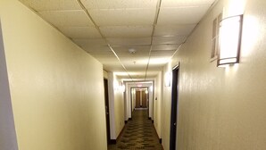 A hotel hallway with carpeted floors and light fixtures on the walls. - Auburn Inn (Auburn)