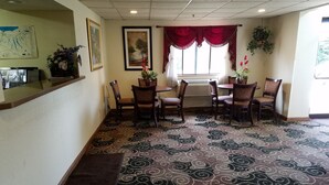 A hotel dining area with a patterned carpet, red curtains, and several chairs. - Auburn Inn (Auburn)