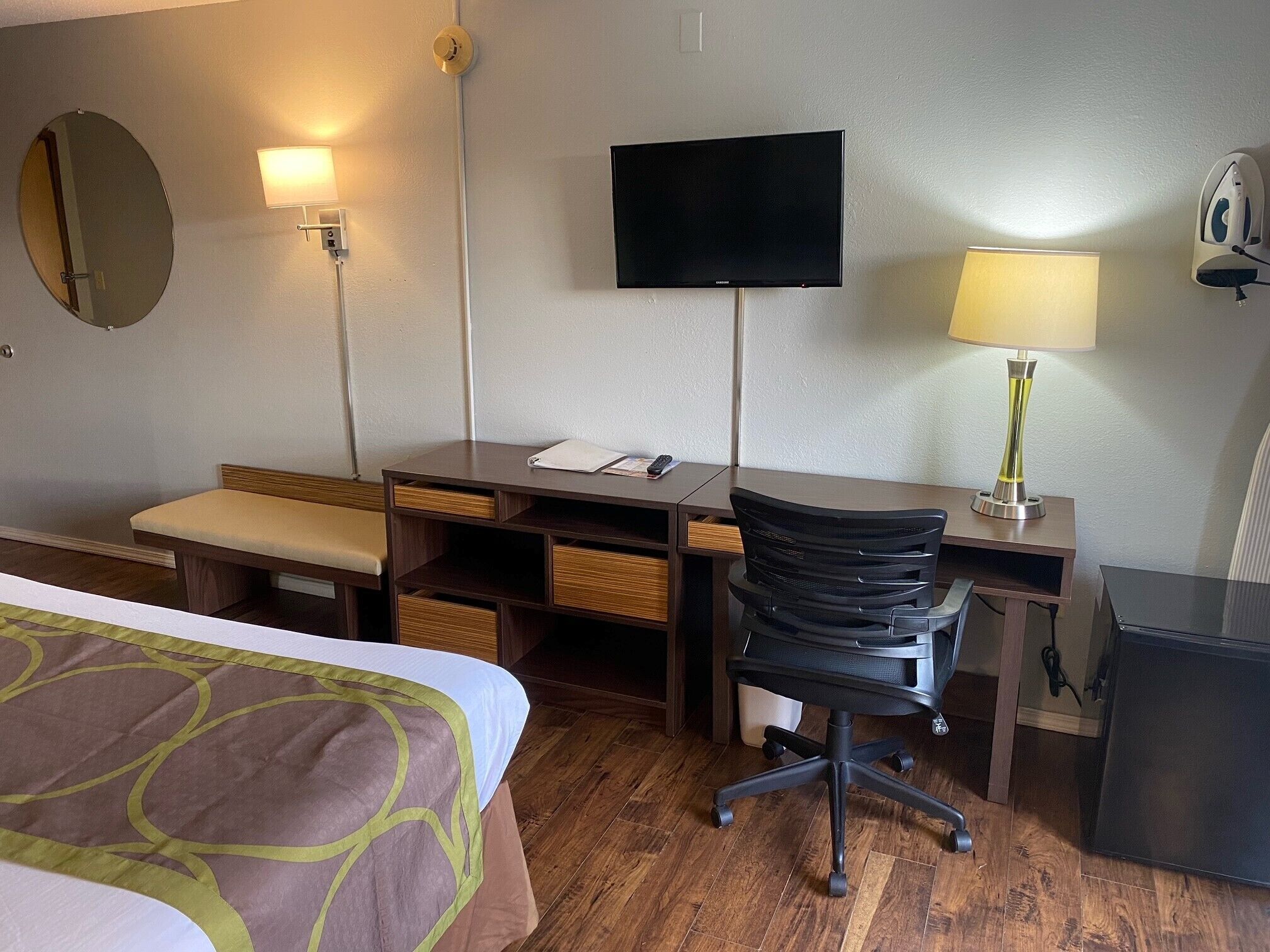 A hotel room with a bed, a desk, a chair, a television, a lamp, and a mirror.
