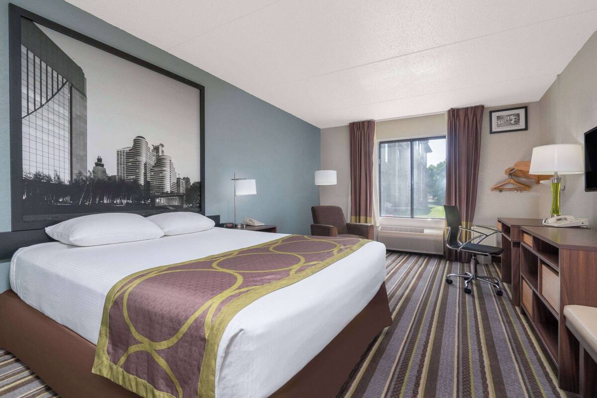 A hotel room with a large bed, a desk, a chair, a TV, and a window with curtains.